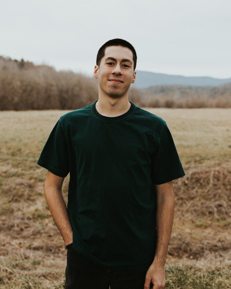 Riley Ridgway smiling in a field, with wooded hills in the background